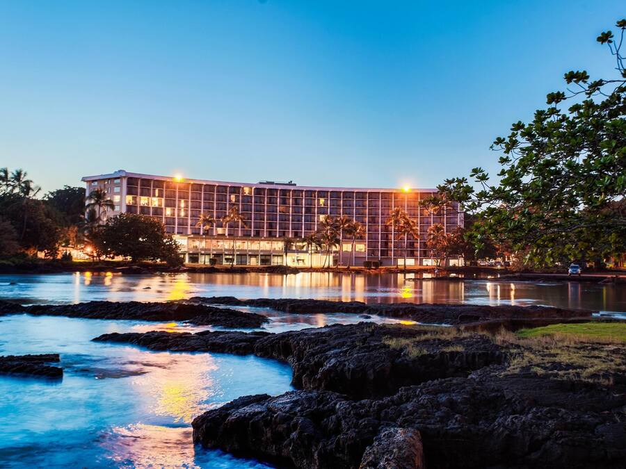 A hotel with a modern architectural design, situated by a body of water with rocky formations.