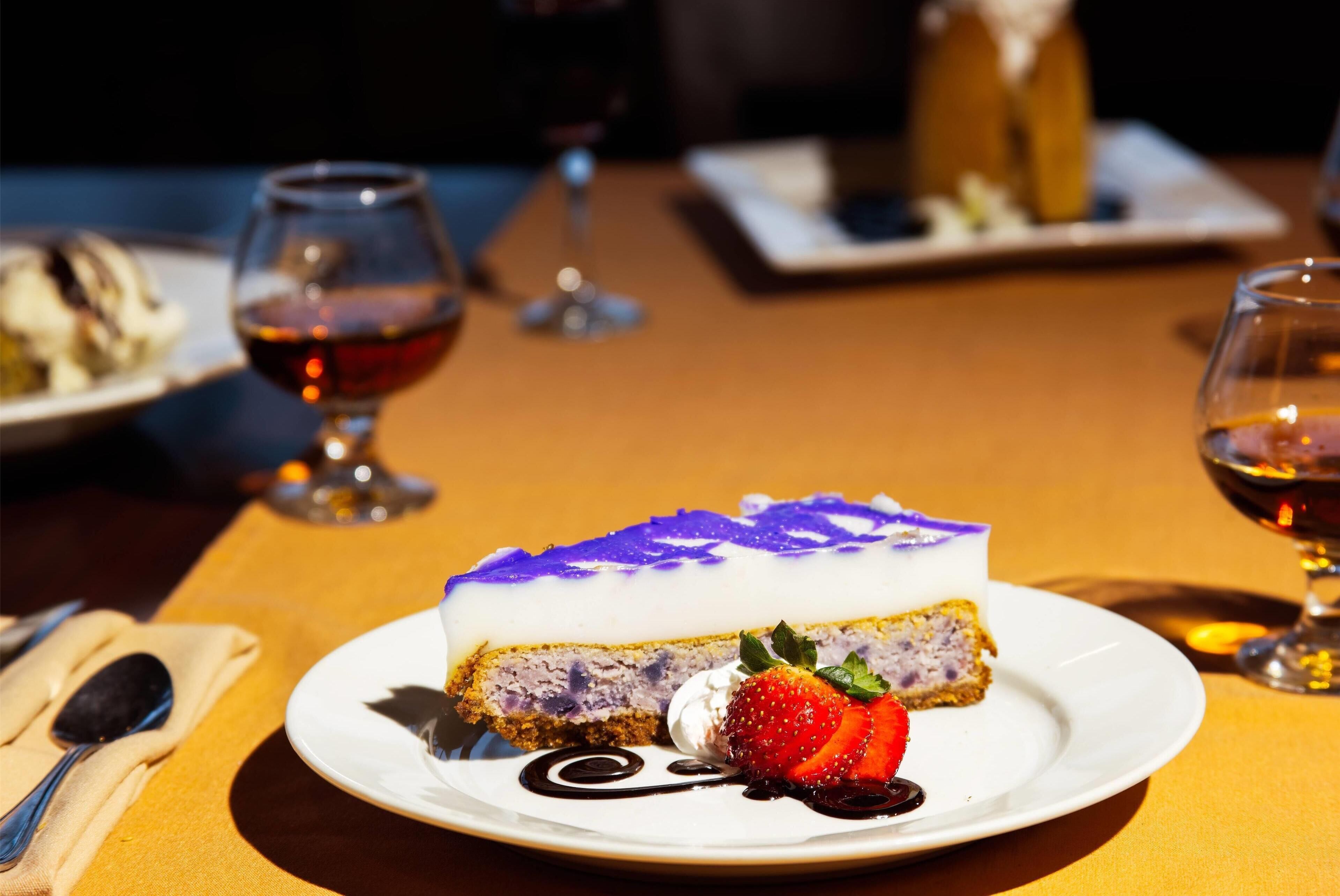 A dessert plate with a slice of cake, a strawberry, and a dollop of whipped cream on a table.