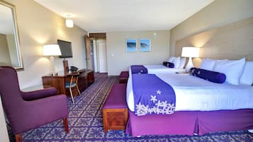 Habitación de hotel con dos camas, un escritorio, una silla y un banco.