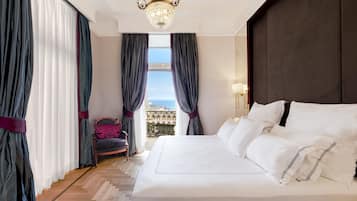 A hotel room with a large bed, a chandelier, a view of the city, and a balcony with curtains.