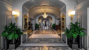 Eine prachtvolle Eingangshalle mit Marmorboden, einer Chandelier und symmetrisch angeordneten Wandleuchten.