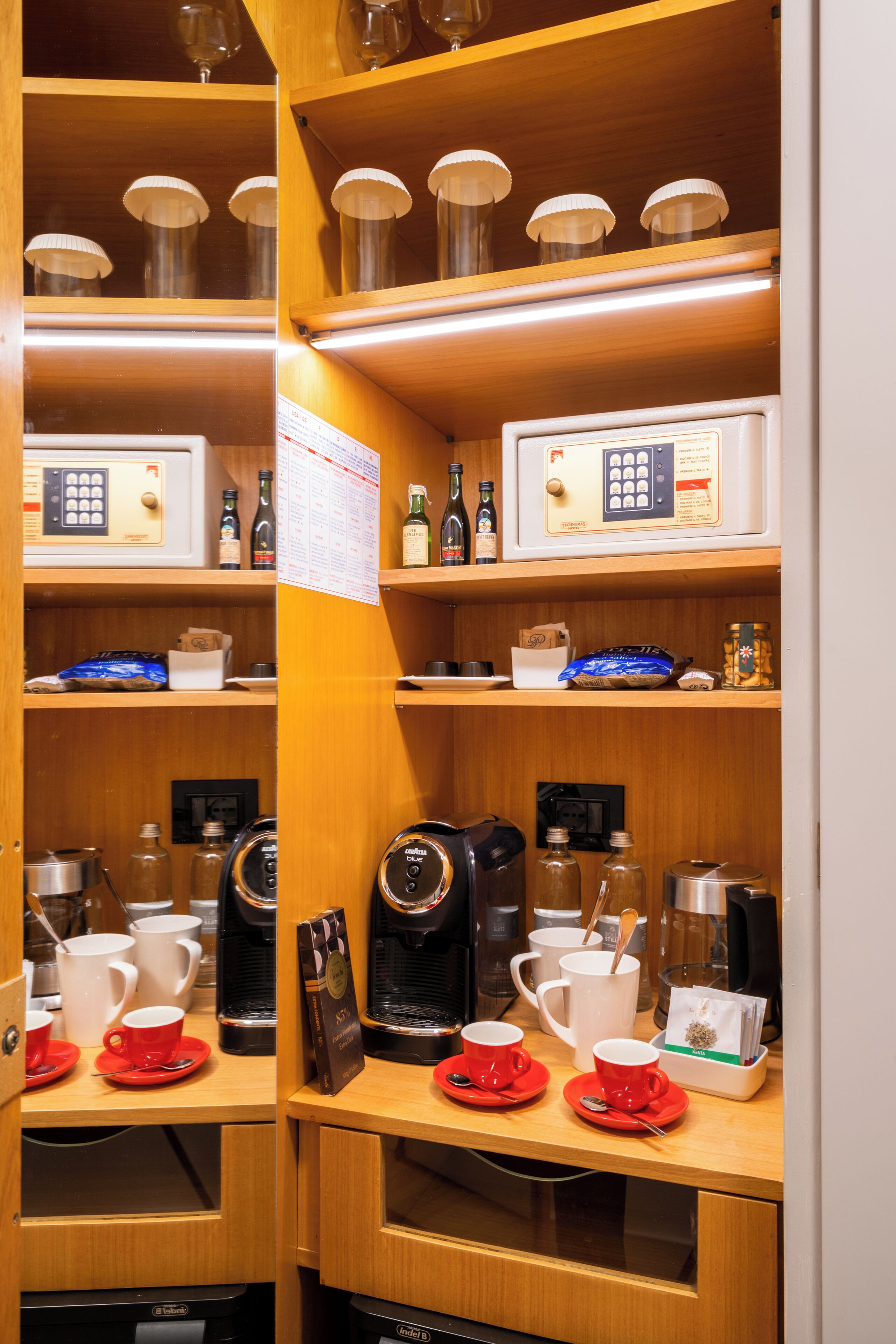 A kitchen with coffee machines, cups, and a refrigerator.