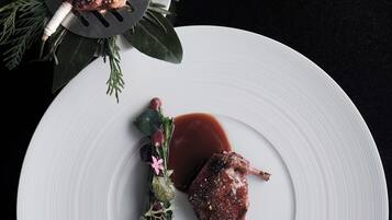 Un plato blanco con carne y salsa, adornado con hierbas y flores, sobre un fondo oscuro.