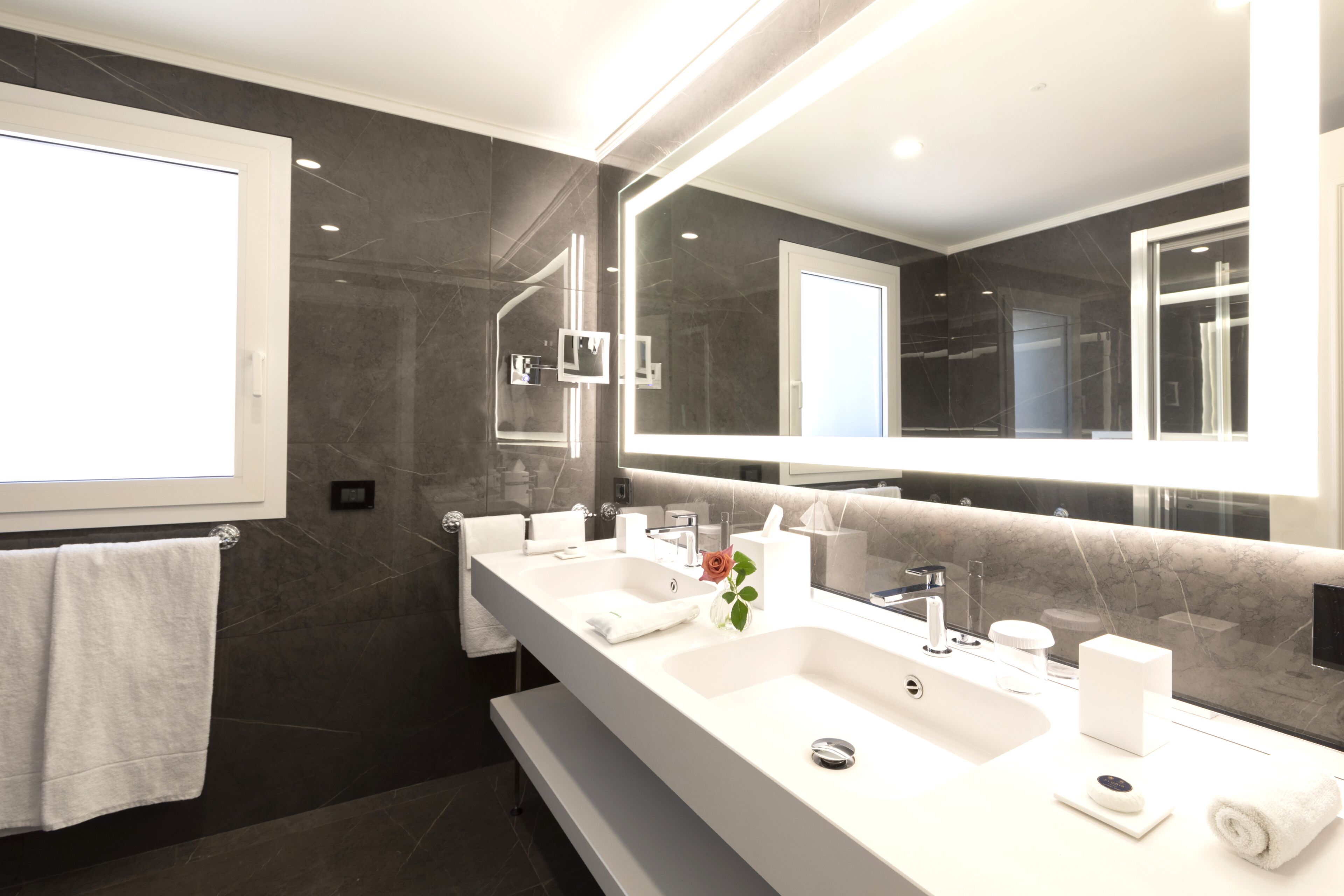 A modern bathroom with two sinks, a large mirror, and a towel rack.