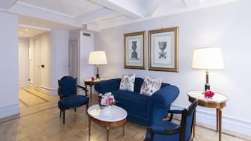 Sala de estar con un sofá azul, dos sillones, una mesa de centro y dos lámparas. Hay cuadros enmarcados en la pared y una puerta al fondo.