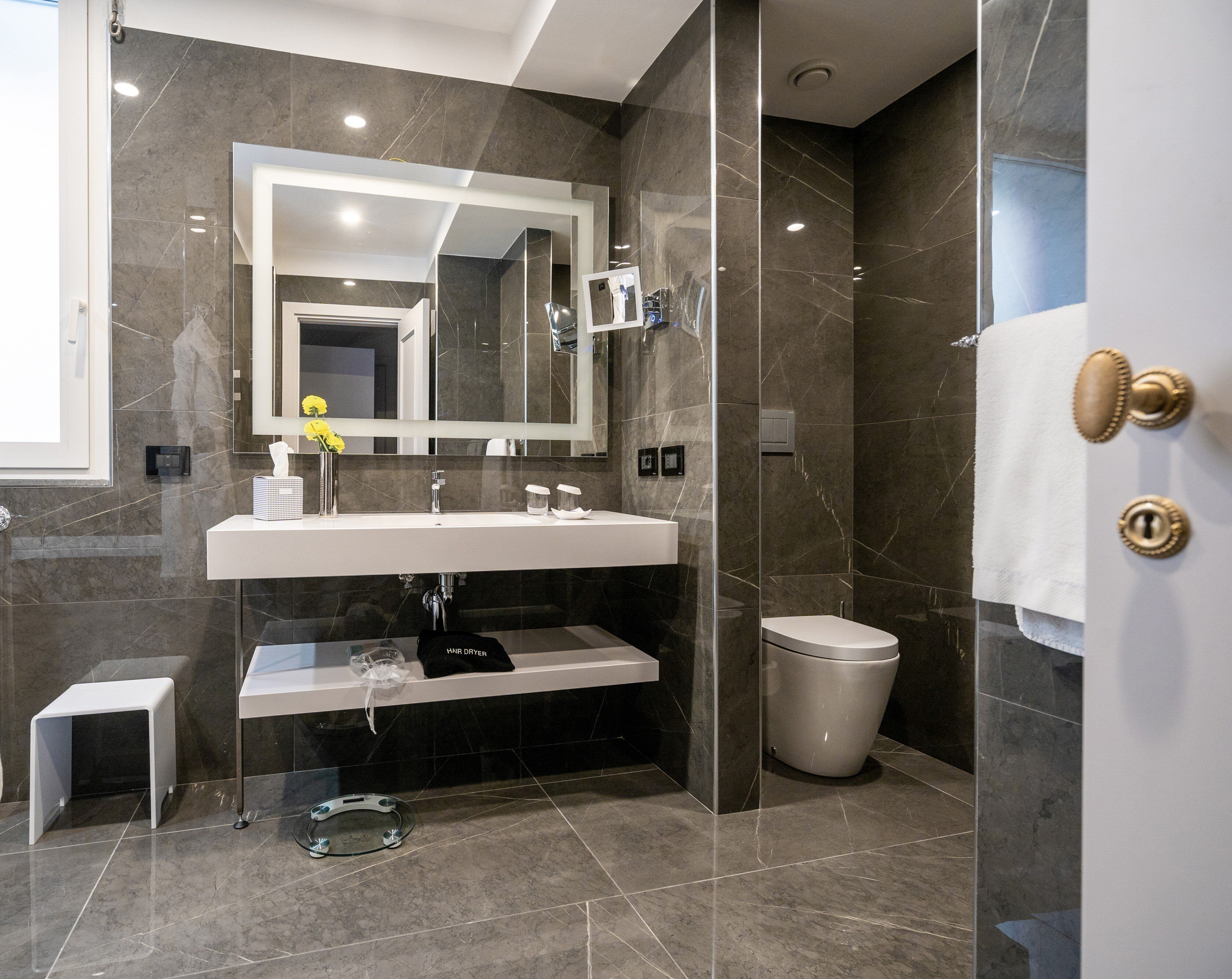 Un baño moderno con un espejo grande, un lavamanos blanco, un inodoro y una cabina de ducha con mampara de cristal.