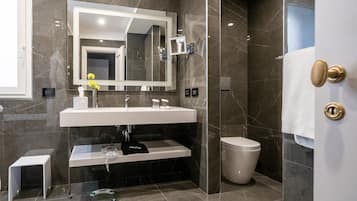 Un baño moderno con un espejo grande, un lavamanos blanco, un inodoro y una cabina de ducha con mampara de cristal.
