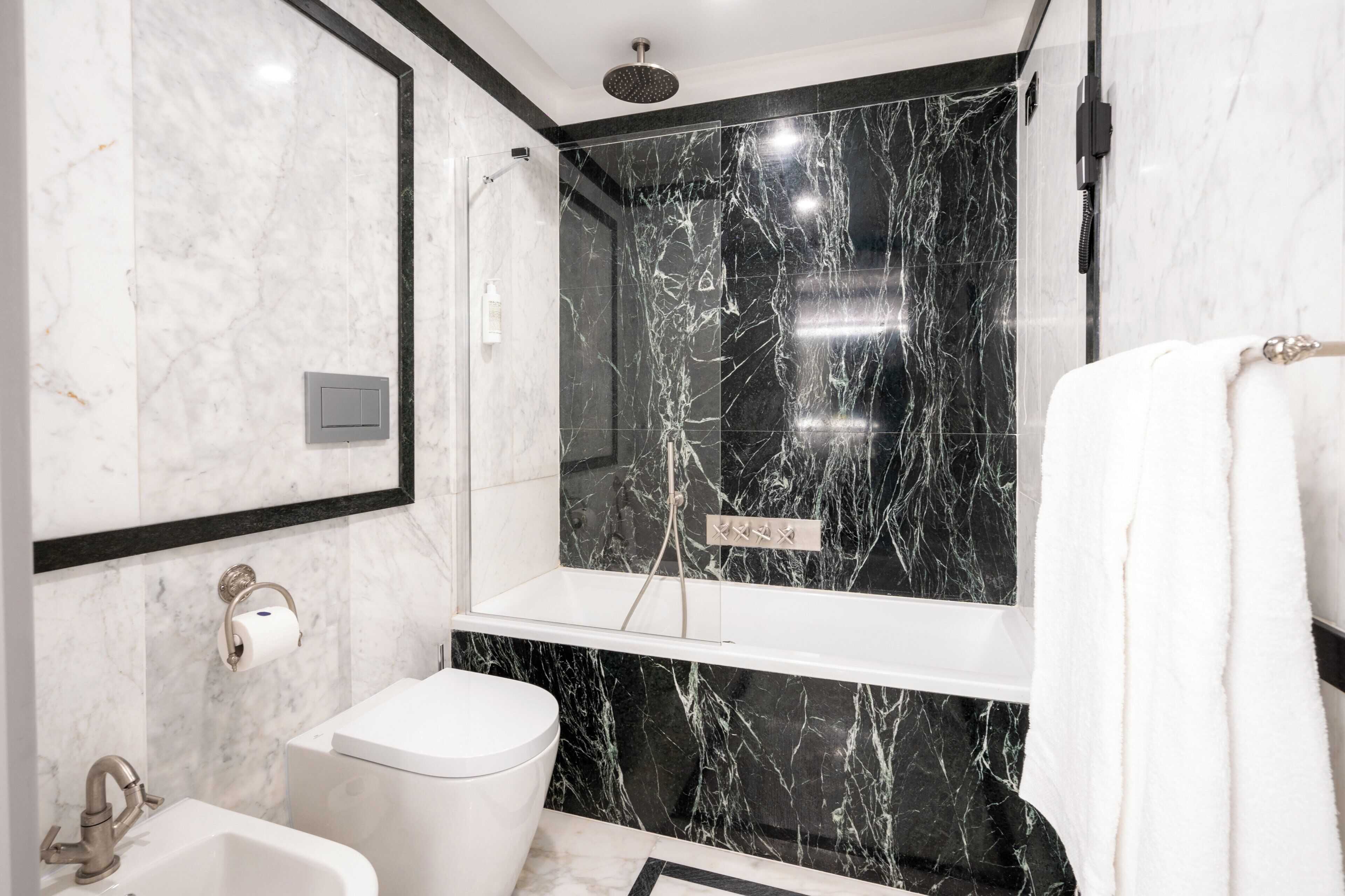 A modern bathroom with a marble shower, a toilet, and a sink.