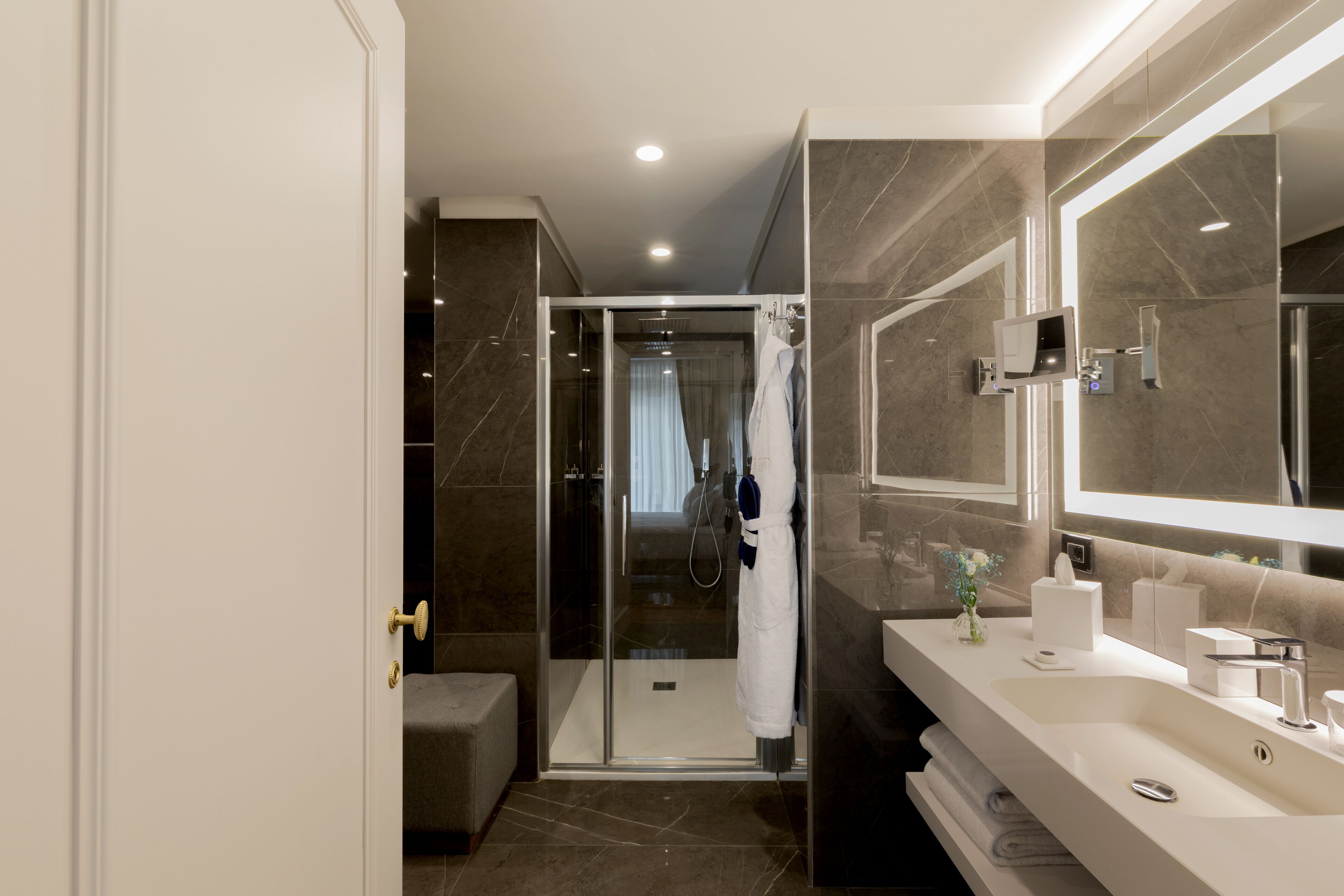 A modern bathroom with a glass shower enclosure, a large mirror, and a vanity with a sink and towel rack.