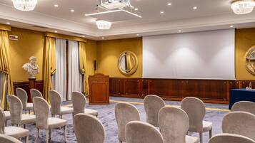 A conference room with rows of chairs, a podium, a projector screen, and a statue.