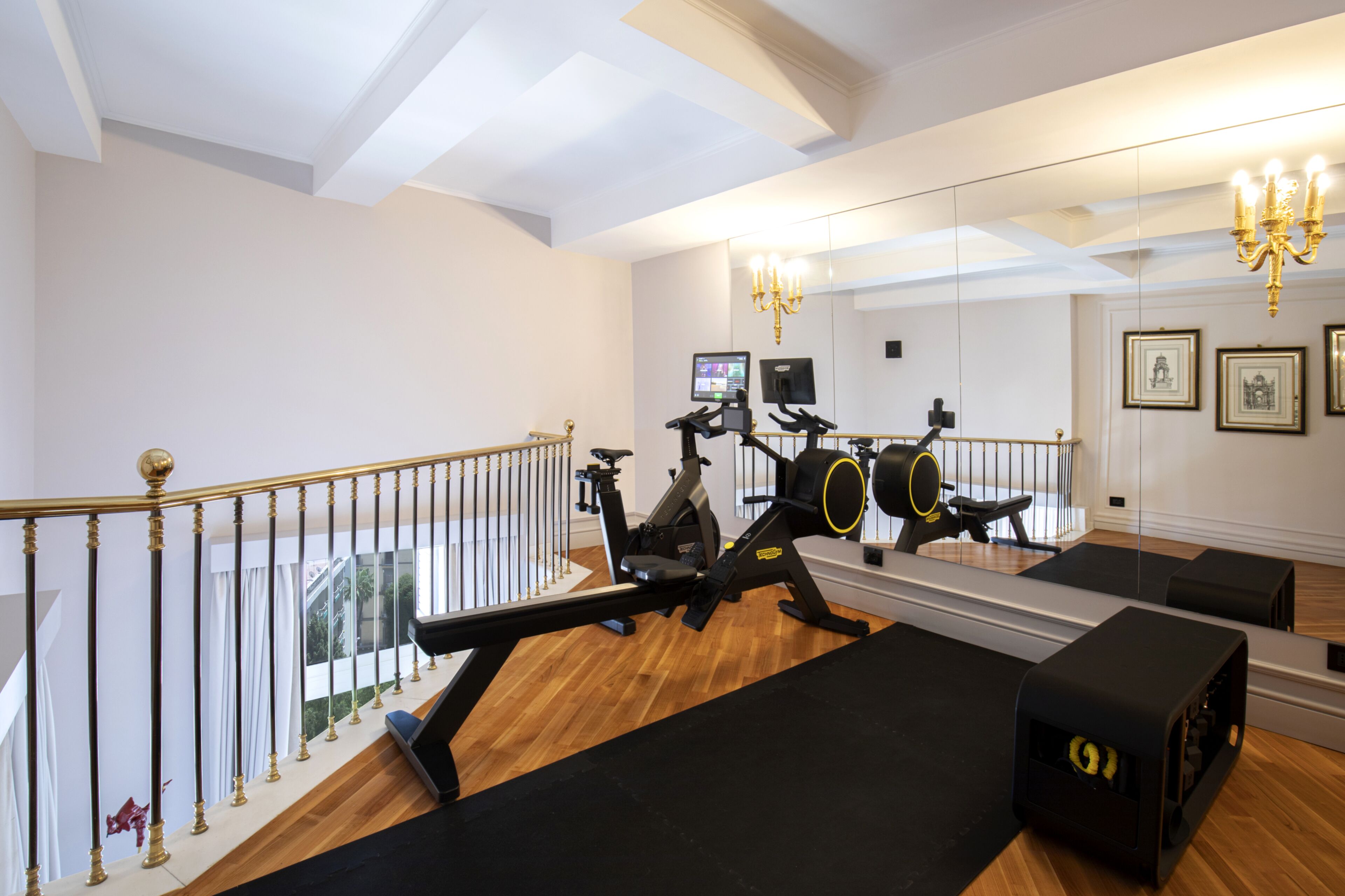 Une salle de sport équipée de matériel d’exercice, dotée d’un grand miroir et d’un lustre.