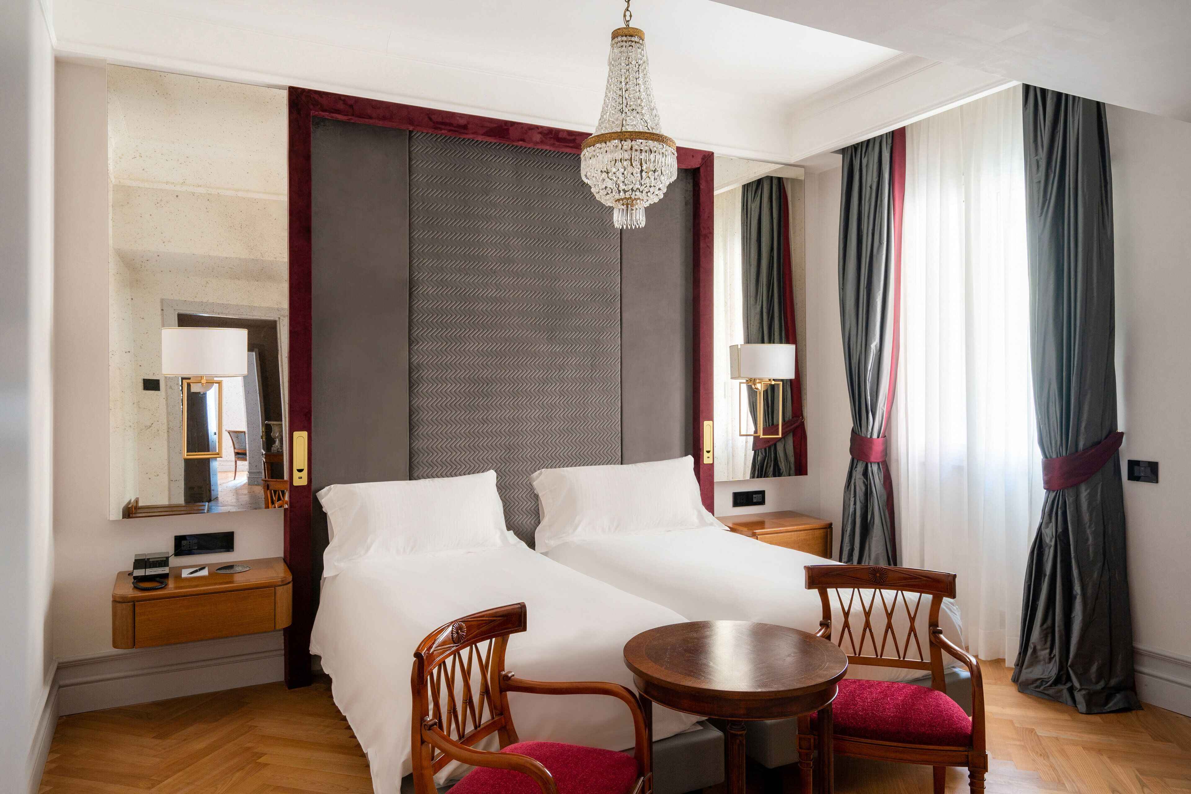 Una habitación de hotel con dos camas, una araña, una mesa de madera y una silla.