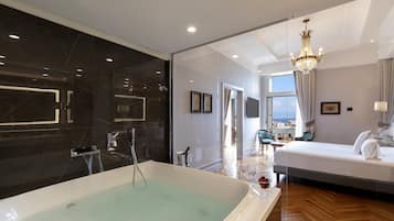 Una habitación de hotel moderna con una bañera grande, una cama, una araña y vistas de la ciudad por la ventana.