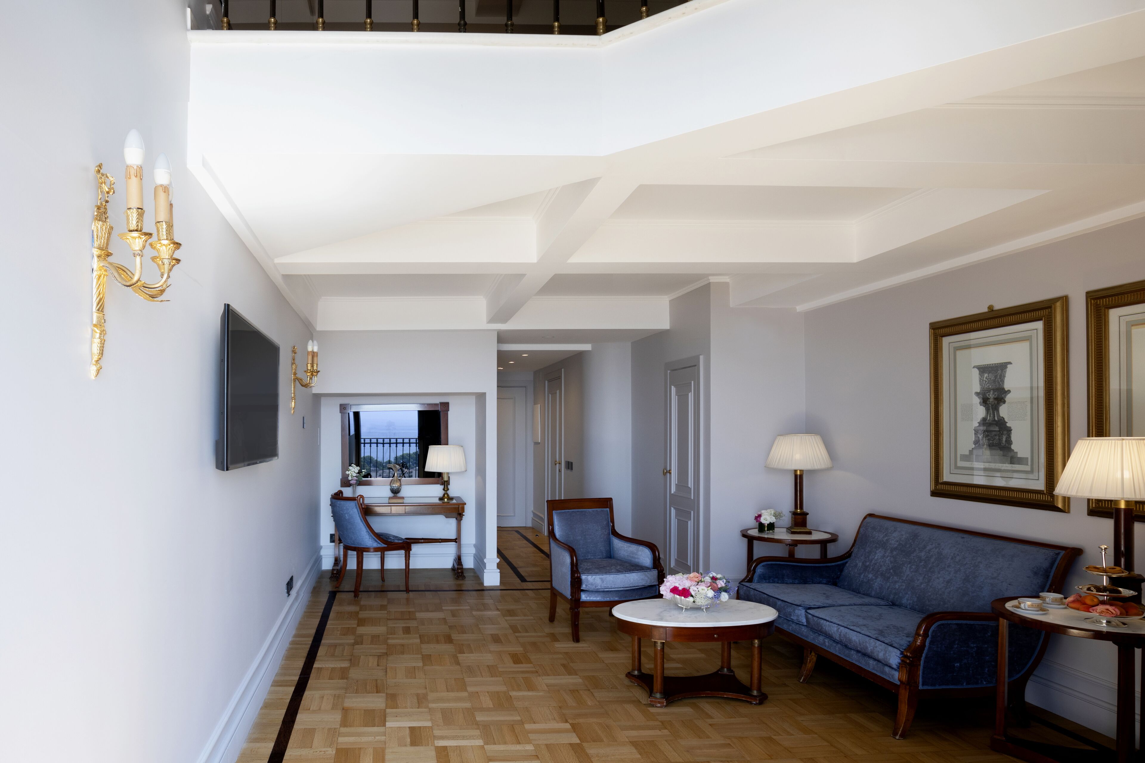 A spacious living room with a high ceiling, a dining area with a chandelier, and a sofa set.
