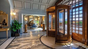 A grand lobby with a marble floor, a large wooden revolving door, and a view of the outdoors through large windows. - Grand Hotel Parkers (Naples)