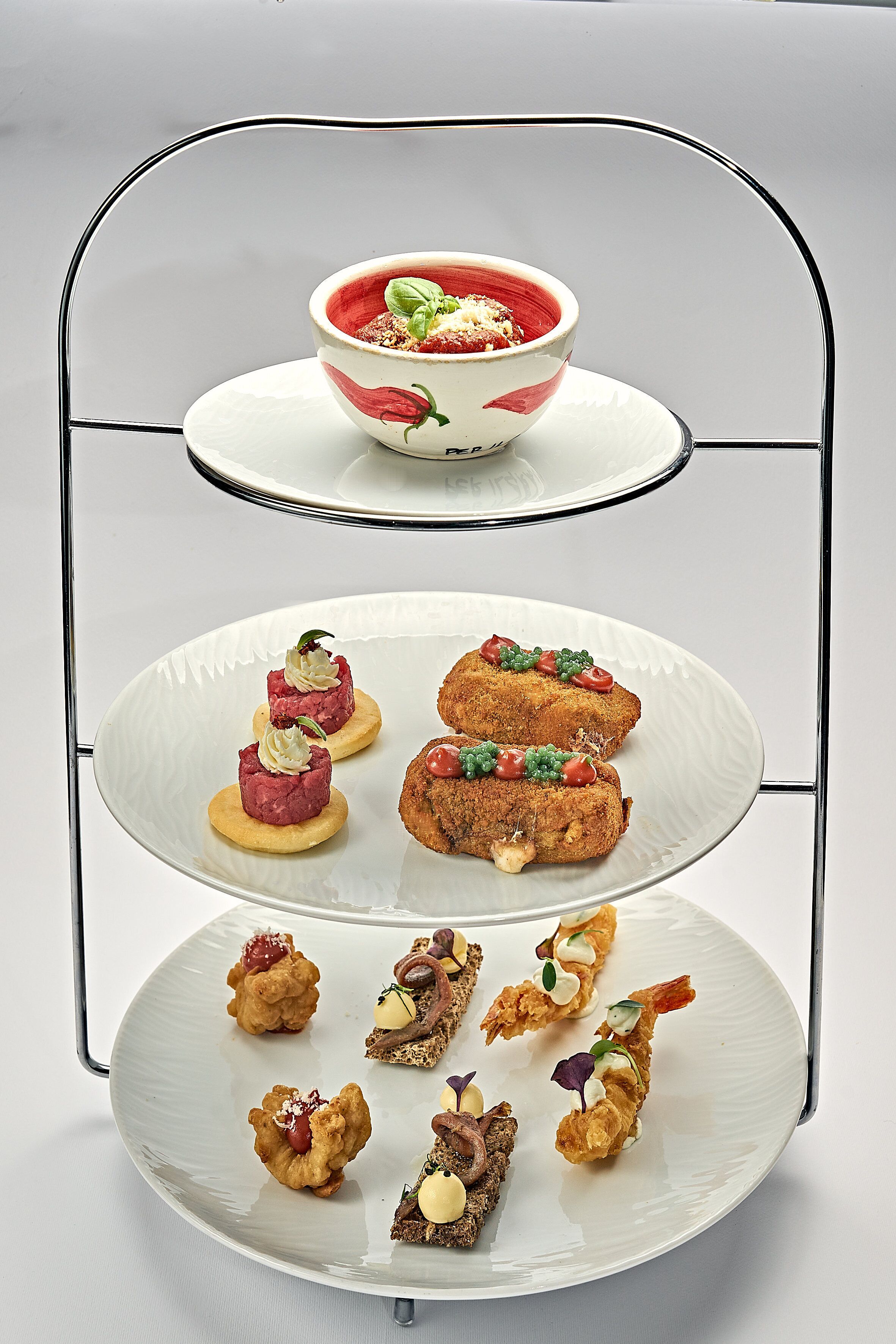 A three-tiered serving tray with various appetizers and a bowl of soup.