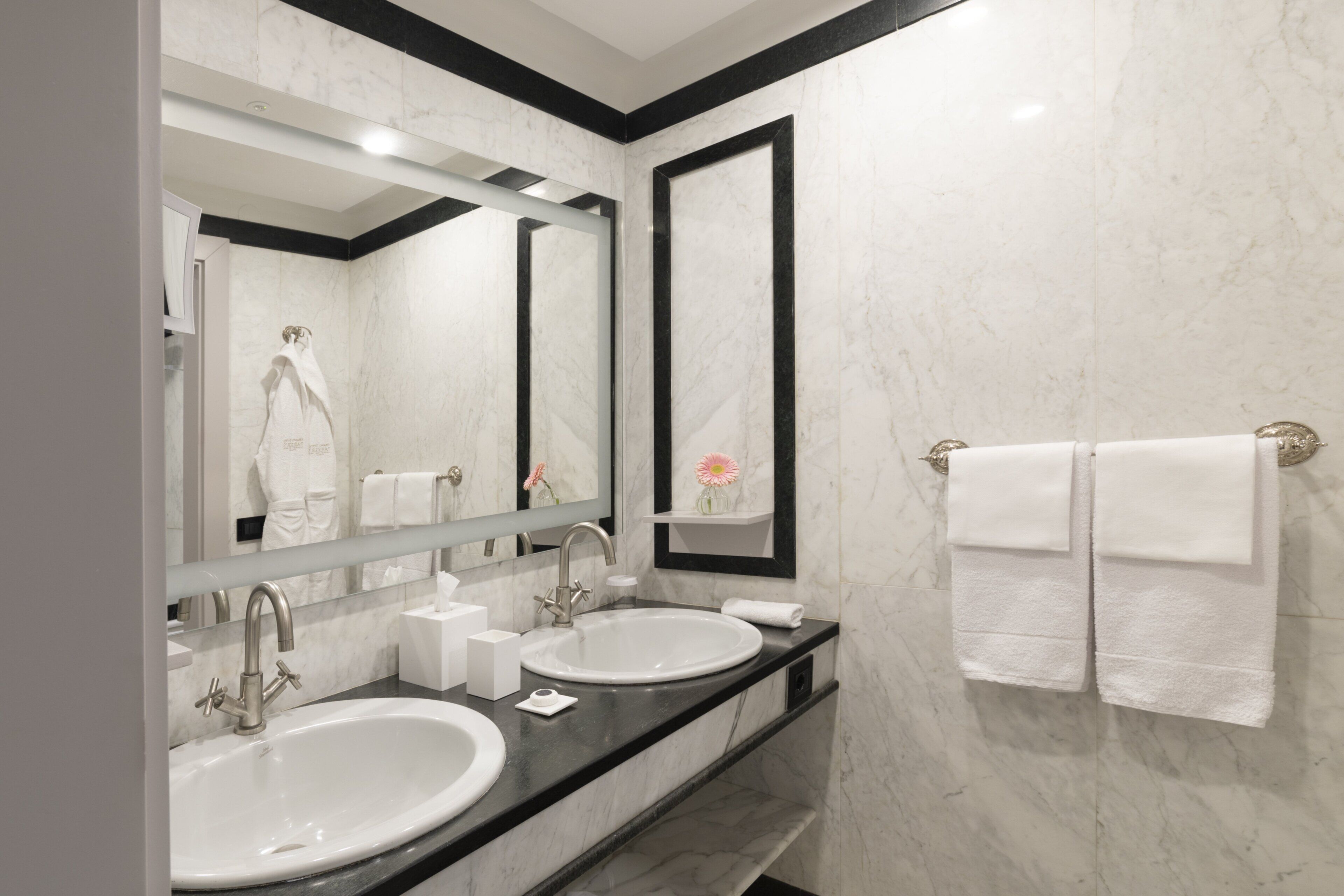 A modern bathroom with two sinks, a large mirror, and a towel rack.