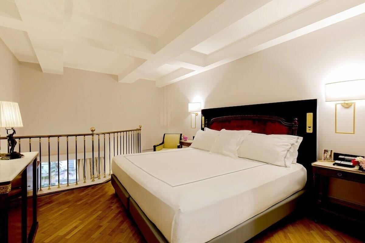 A hotel room with a large bed, a desk with a lamp, a chair, and a view of the outdoors.