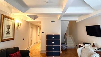 A spacious living room with a black sofa, a white armchair, and a marble coffee table. There is a blue chest of drawers and a staircase leading to another level.