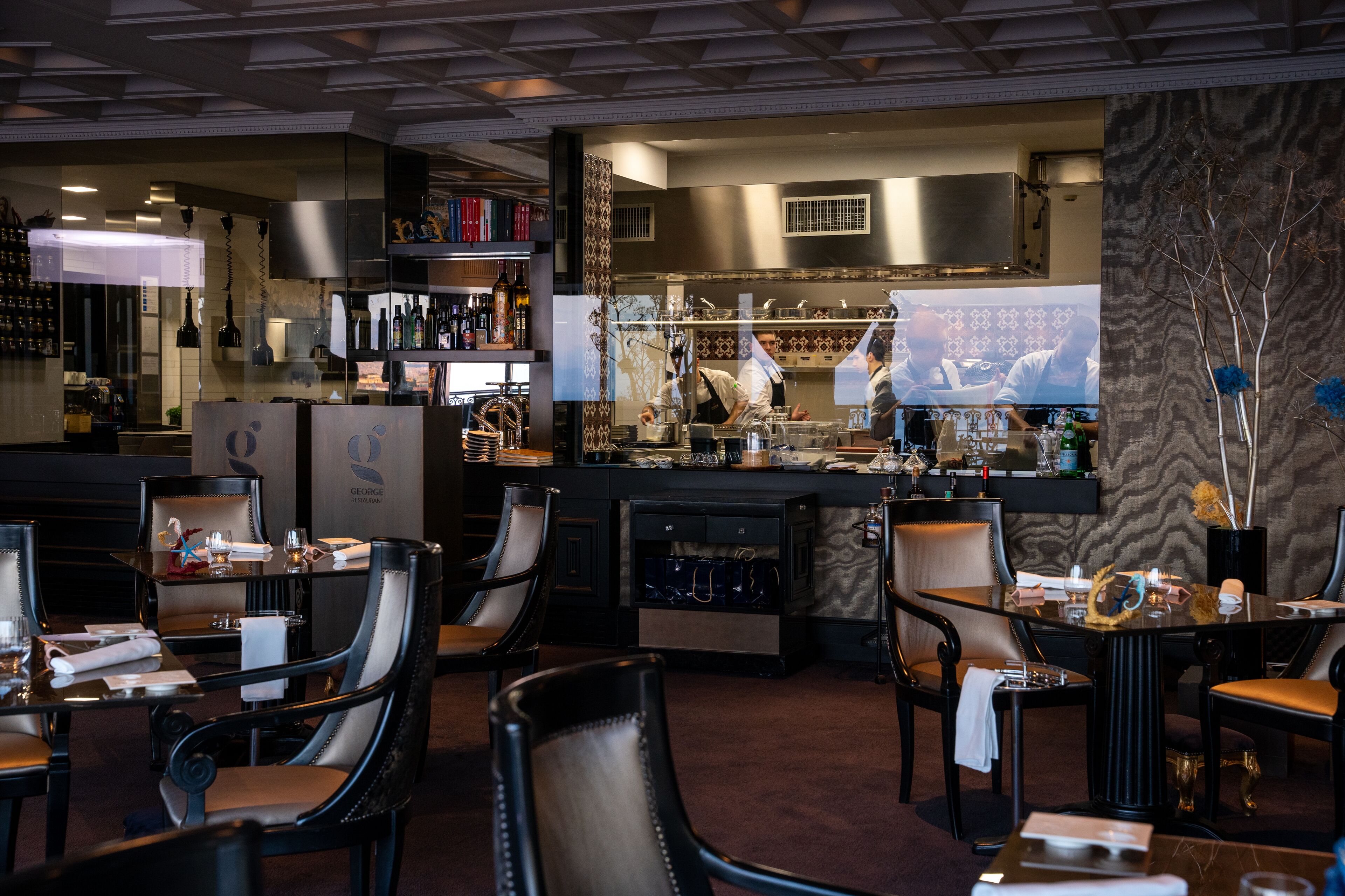A restaurant with a bar area, multiple seating arrangements, and a visible kitchen in the background.