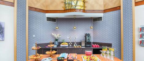 A hotel room with a breakfast buffet, a coffee machine, and a decorative vase with flowers.
