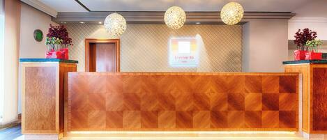Un comptoir d’accueil d’hôtel avec un panneau décoratif en bois, deux lampes suspendues sphériques et un panneau mural.