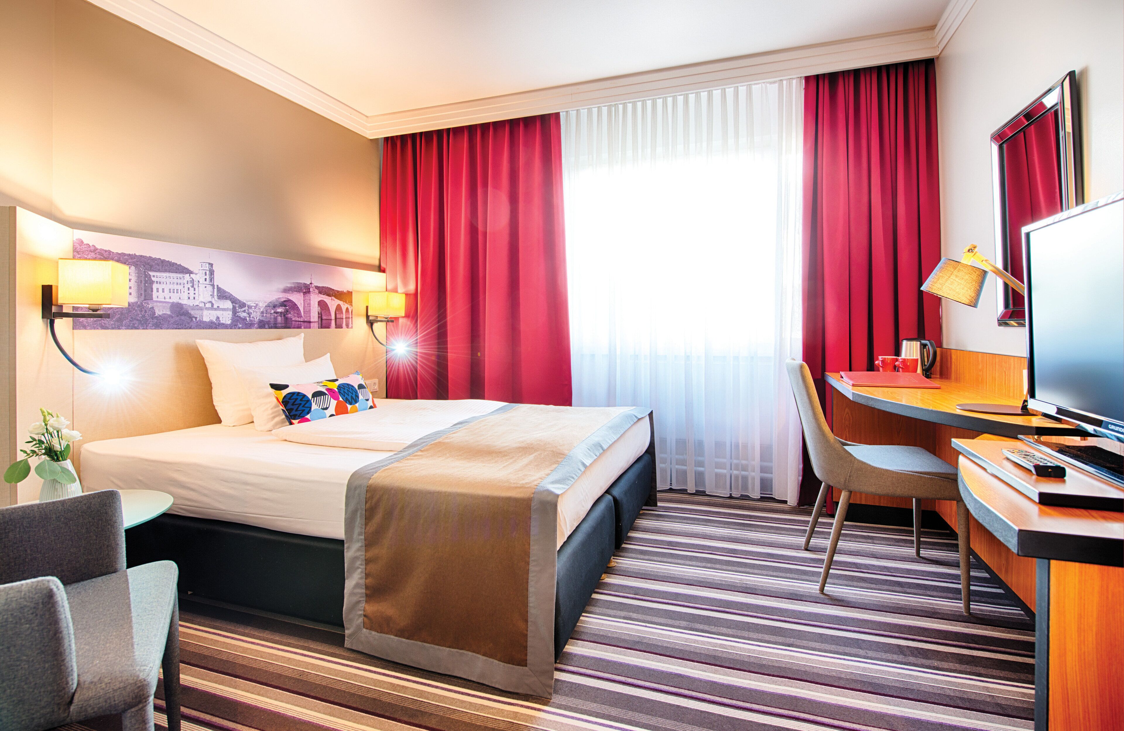Ein Hotelzimmer mit Bett, Schreibtisch, Stuhl, Fernseher und einem Bild an der Wand.