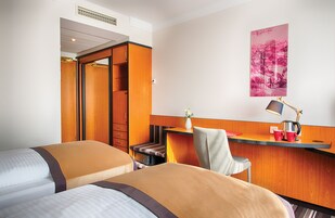 Een hotelkamer met twee bedden, een bureau met lamp, een stoel, een klein tafeltje en een poster aan de muur.