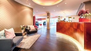 A modern hotel lobby with a reception desk, seating area, and a large window providing a view of the interior. - Leonardo Hotel Heidelberg (Heidelberg)