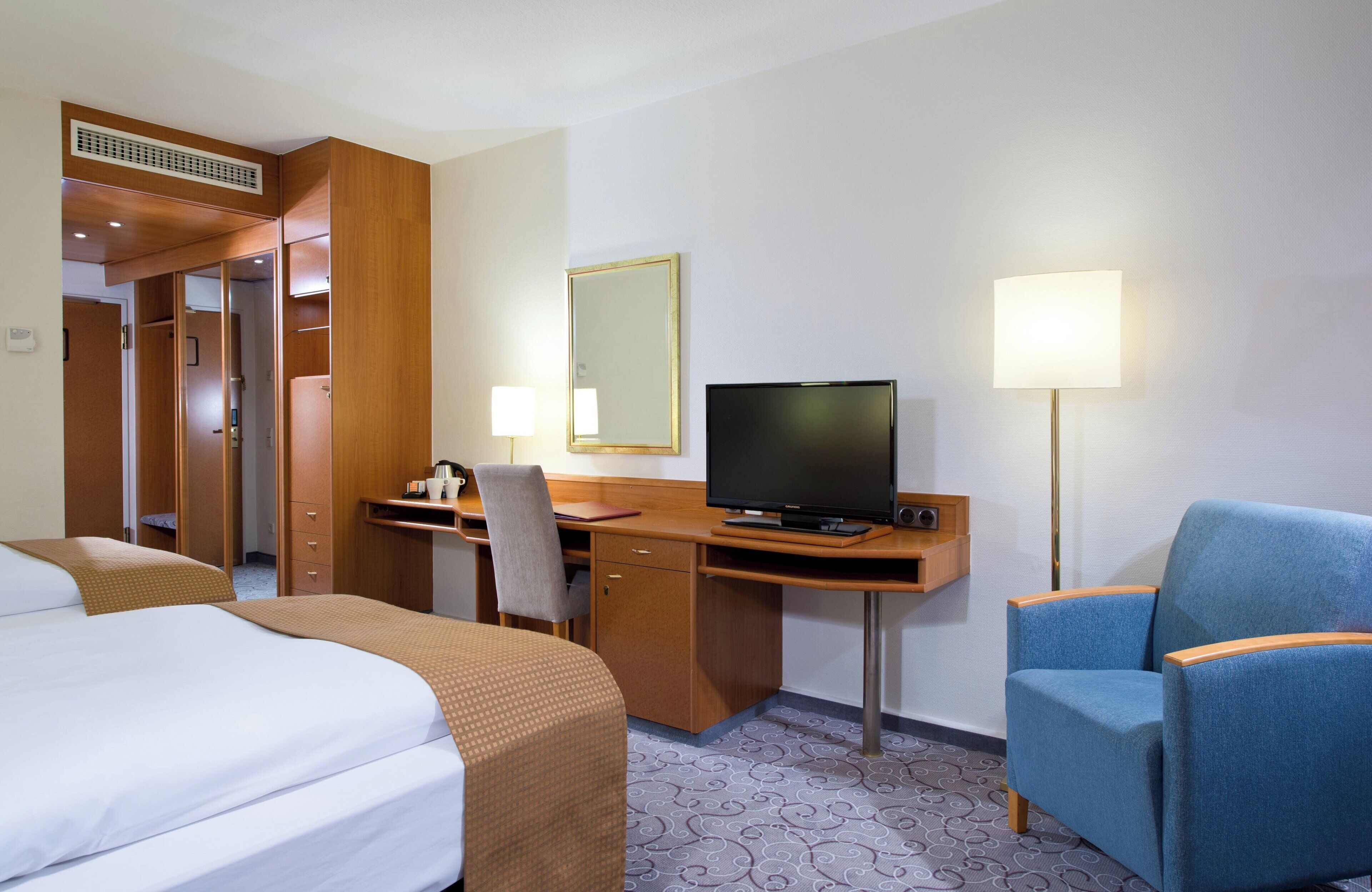 A hotel room with a bed, desk, chair, television, and two lamps.