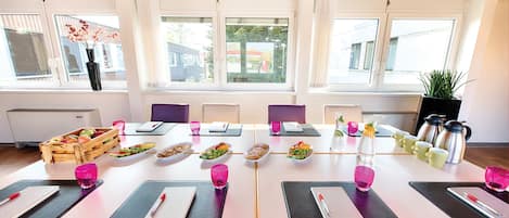 A conference room with a long table set for a meeting, equipped with laptops, notebooks, and cups.