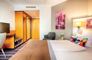 A hotel room with a bed, a desk, a chair, a TV, and a staircase leading to a closet. - Leonardo Hotel Heidelberg (Heidelberg)