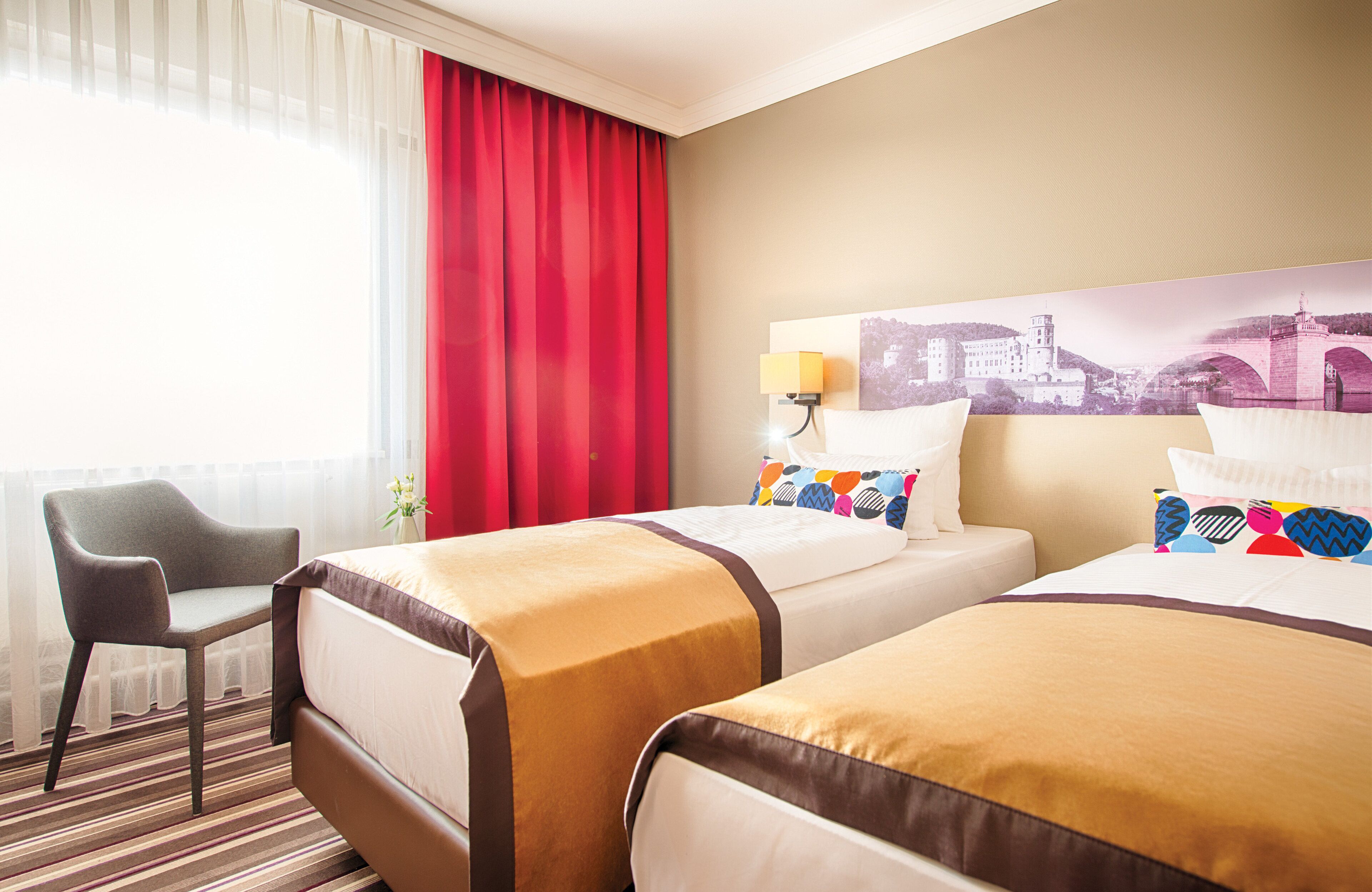 A hotel room with two beds, a chair, a lamp, and a window with curtains.