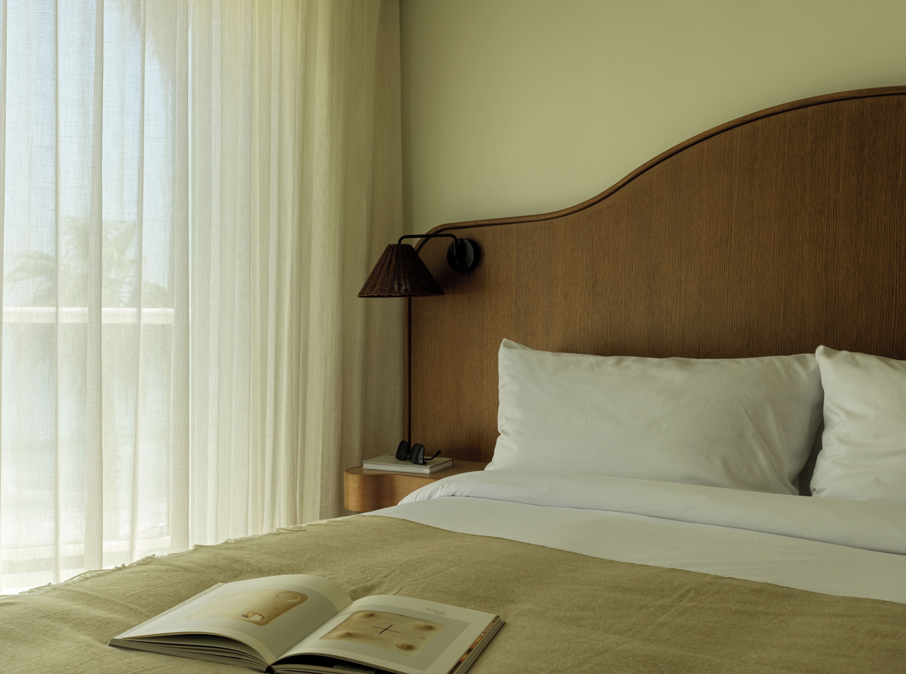 A neatly made bed with white linens, a wooden headboard, and a lamp on a bedside table.