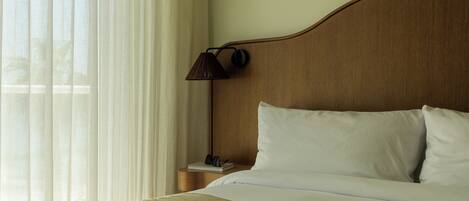 A neatly made bed with white linens, a wooden headboard, and a lamp on a bedside table.