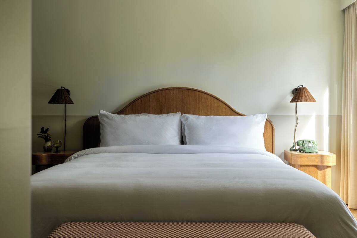 A neatly made bed with white linens, a wooden headboard, and two bedside tables with lamps and a telephone.