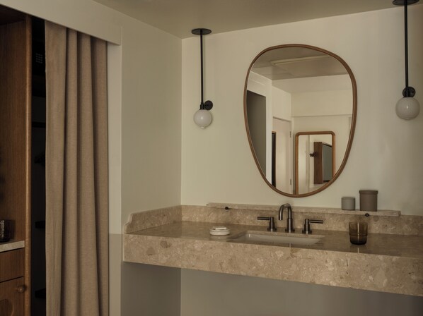 A bathroom with a marble sink, a round mirror, and two pendant lights.