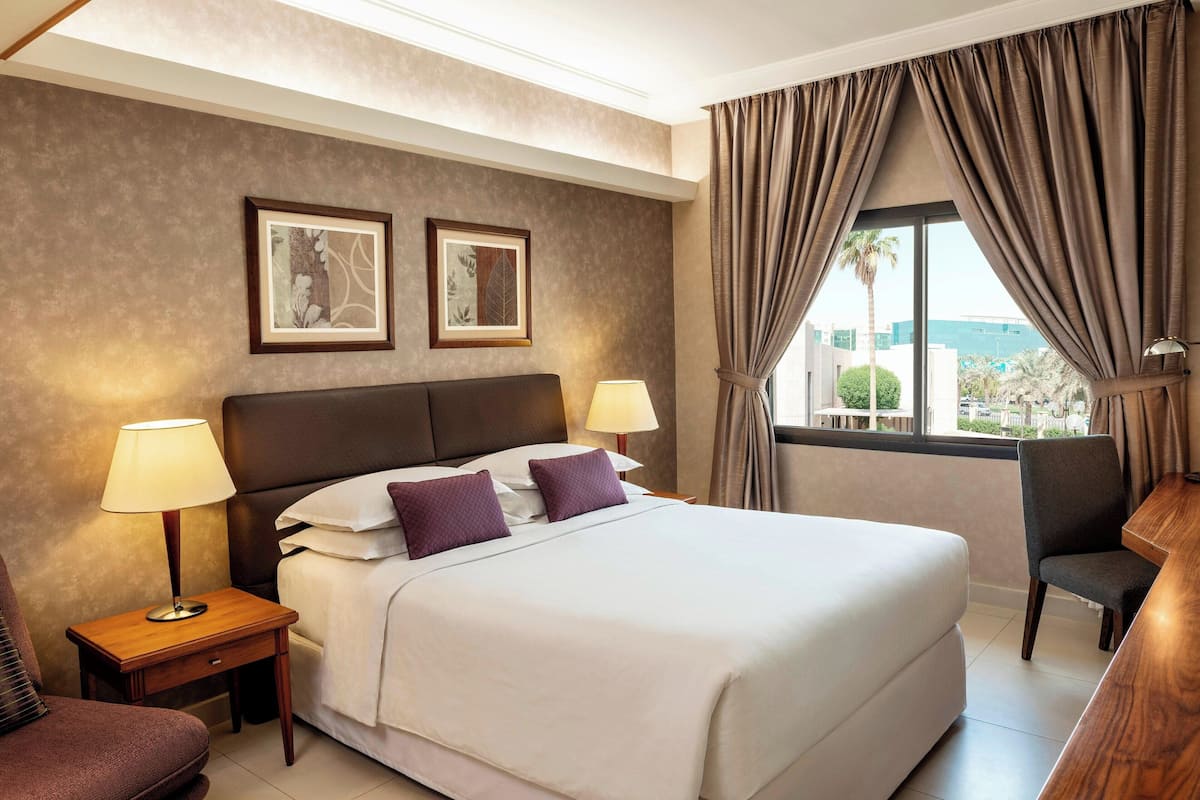 A hotel room with a large bed, two bedside lamps, a chair, and a desk.