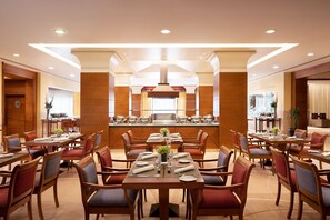 A spacious dining area with multiple tables and chairs, a central kitchen area, and a modern ceiling design.