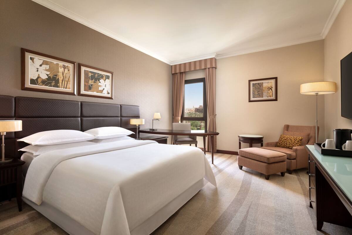 A hotel room with a large bed, a desk, a chair, and a television.