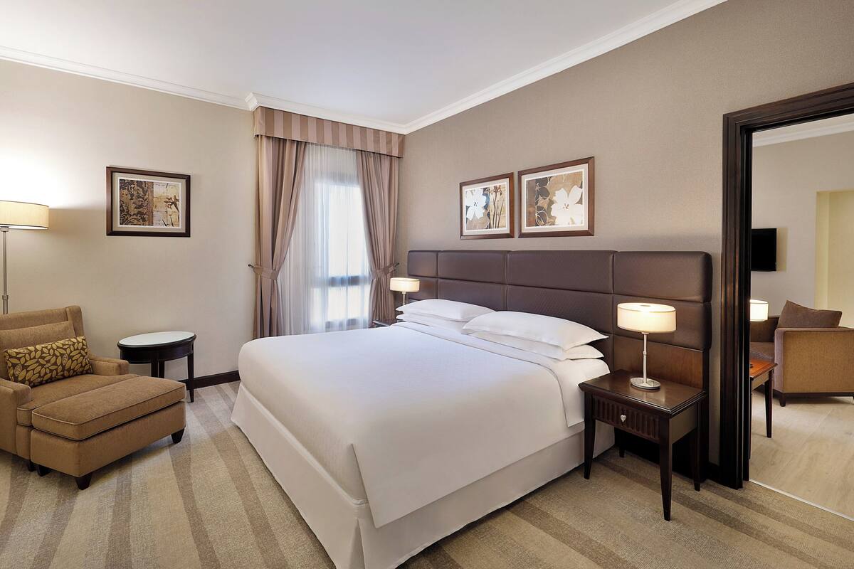 A hotel room with a large bed, a chair, a nightstand, and a mirror.
