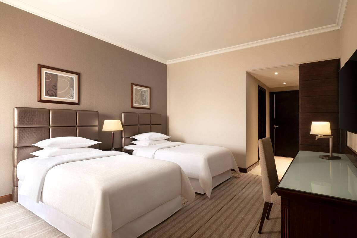 A hotel room with two beds, a desk, and a chair.