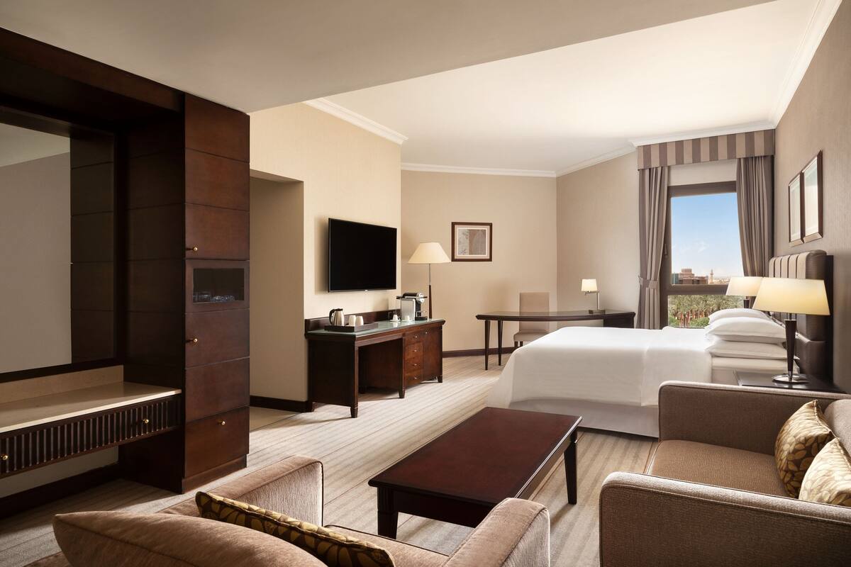 A hotel room with a bed, a desk, a television, a coffee maker, and a sofa.