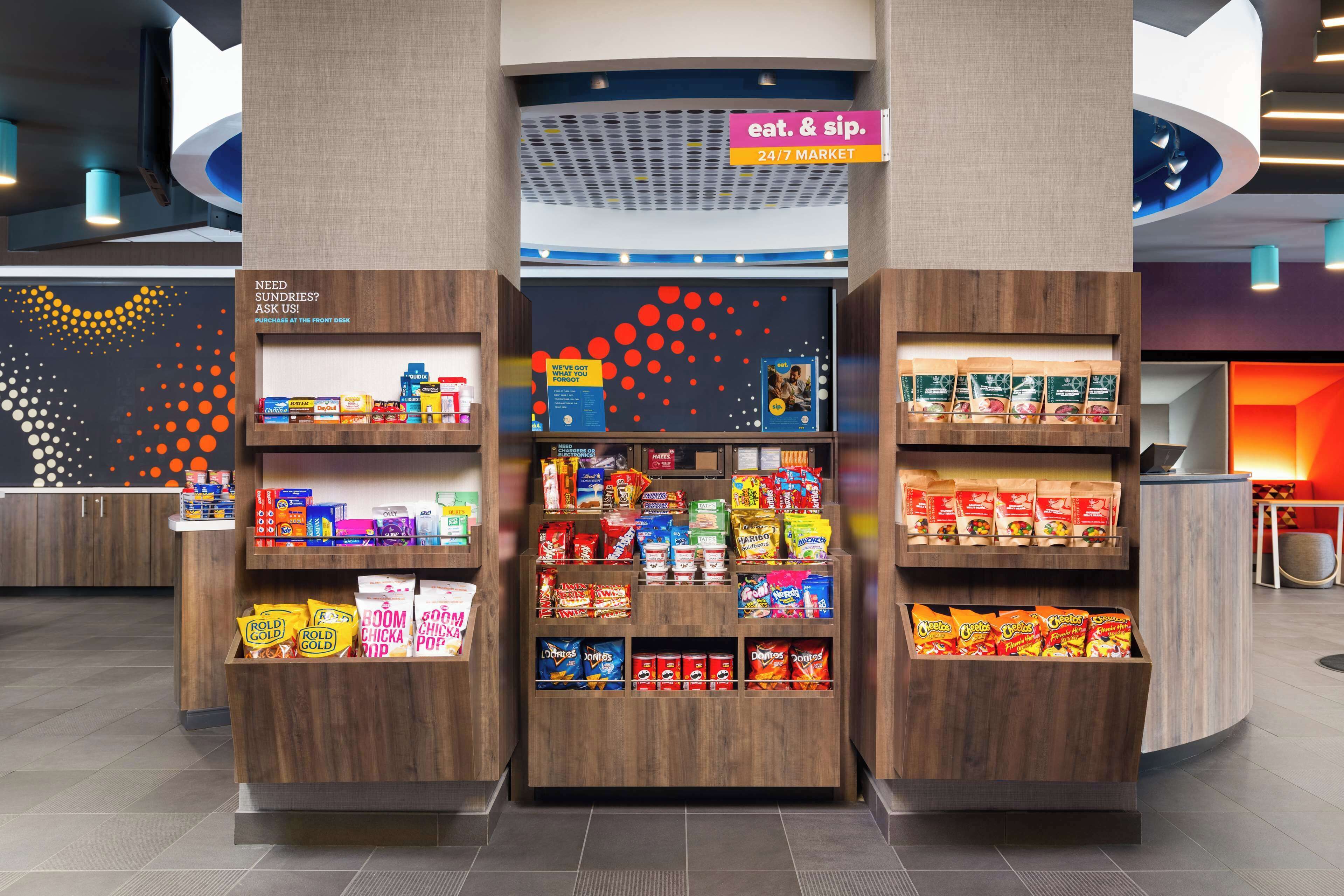A snack kiosk with a variety of packaged snacks, a 24/7 market sign, and a 'Need Sundries?' sign.
