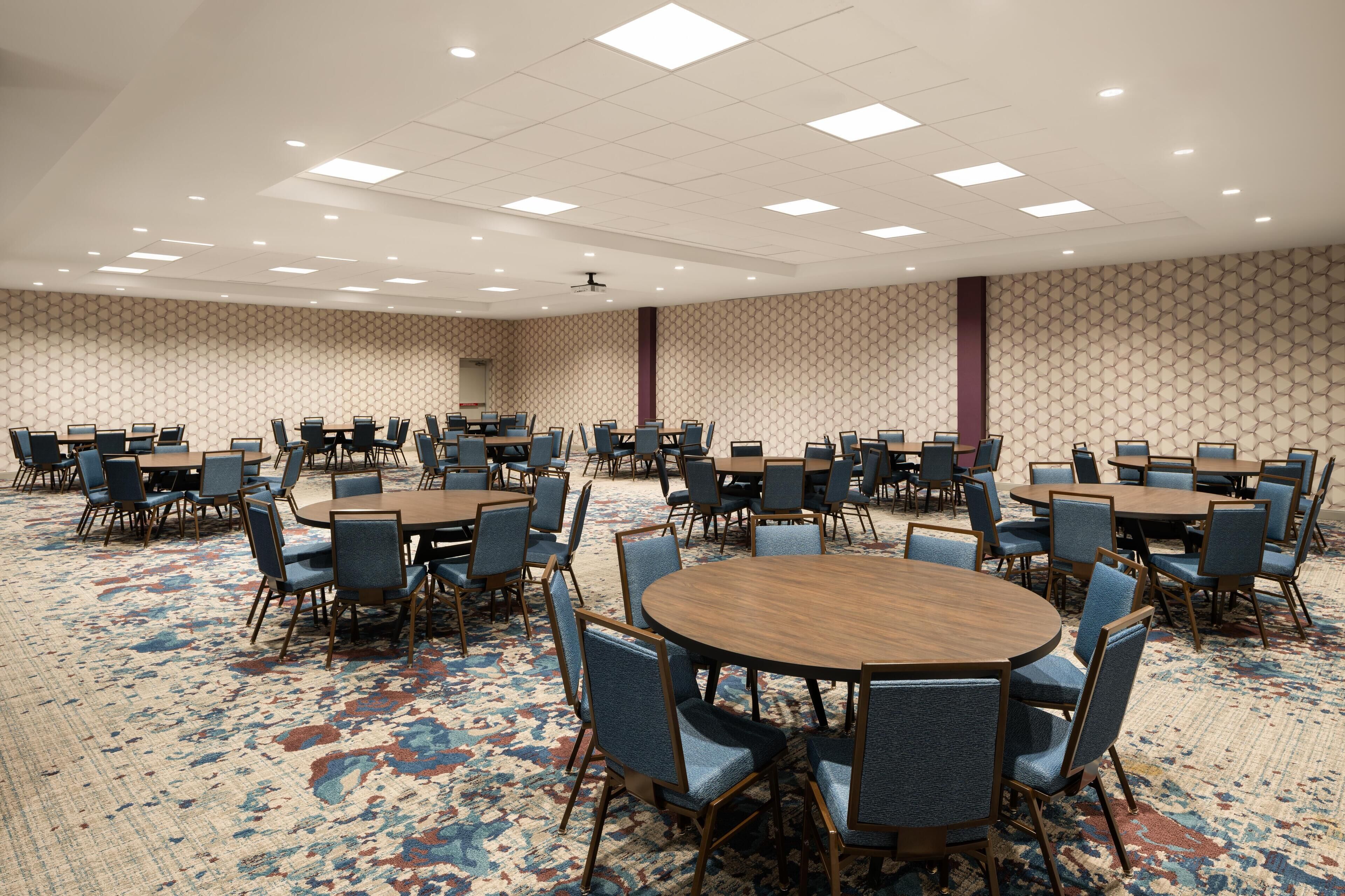 A conference room with multiple tables and chairs, carpeted floor, and patterned wall design.