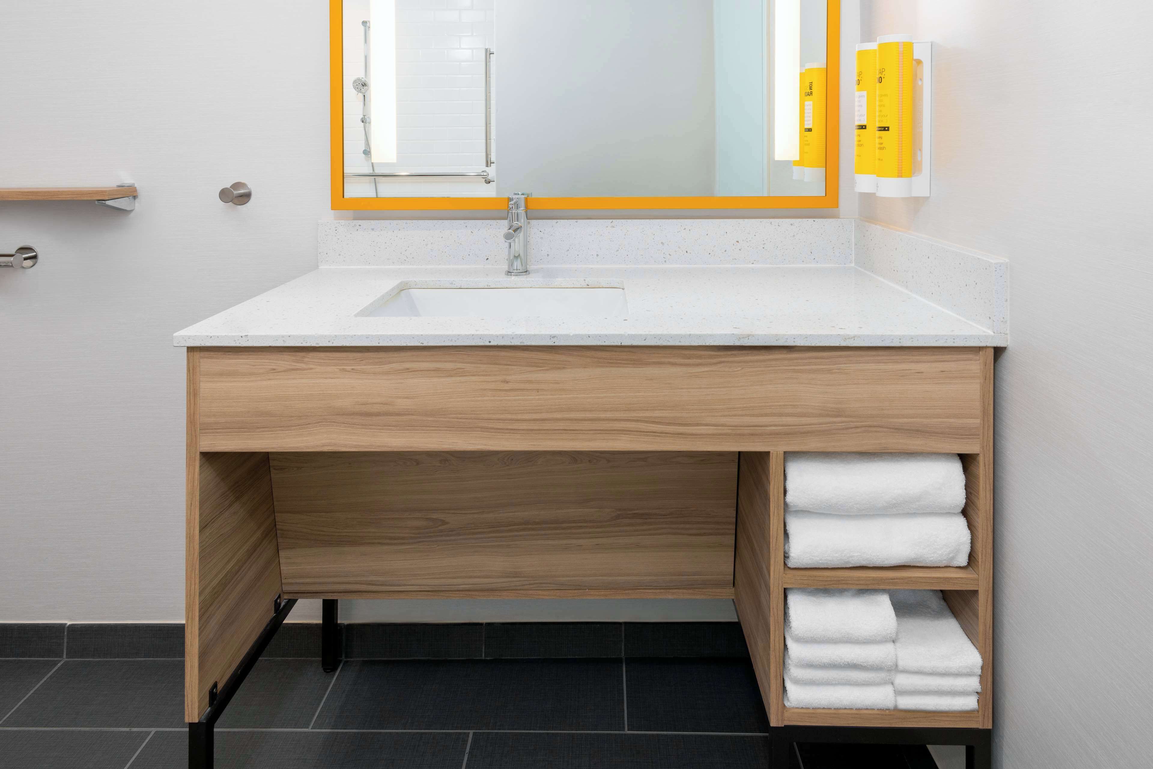 Un bagno moderno con un lavandino bianco, un mobile vanità in legno e uno specchio con cornice arancione.