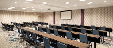 A conference room with long tables and chairs, a carpeted floor, and a projector screen on the wall.