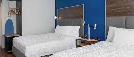 Habitación de hotel con dos camas, piso de madera, pared azul y perchero con ganchos.