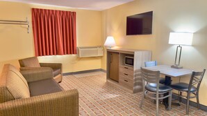A hotel room with a sofa, a desk, a chair, a TV, and a lamp. - Econo Lodge Lansing - Leavenworth (Lansing)