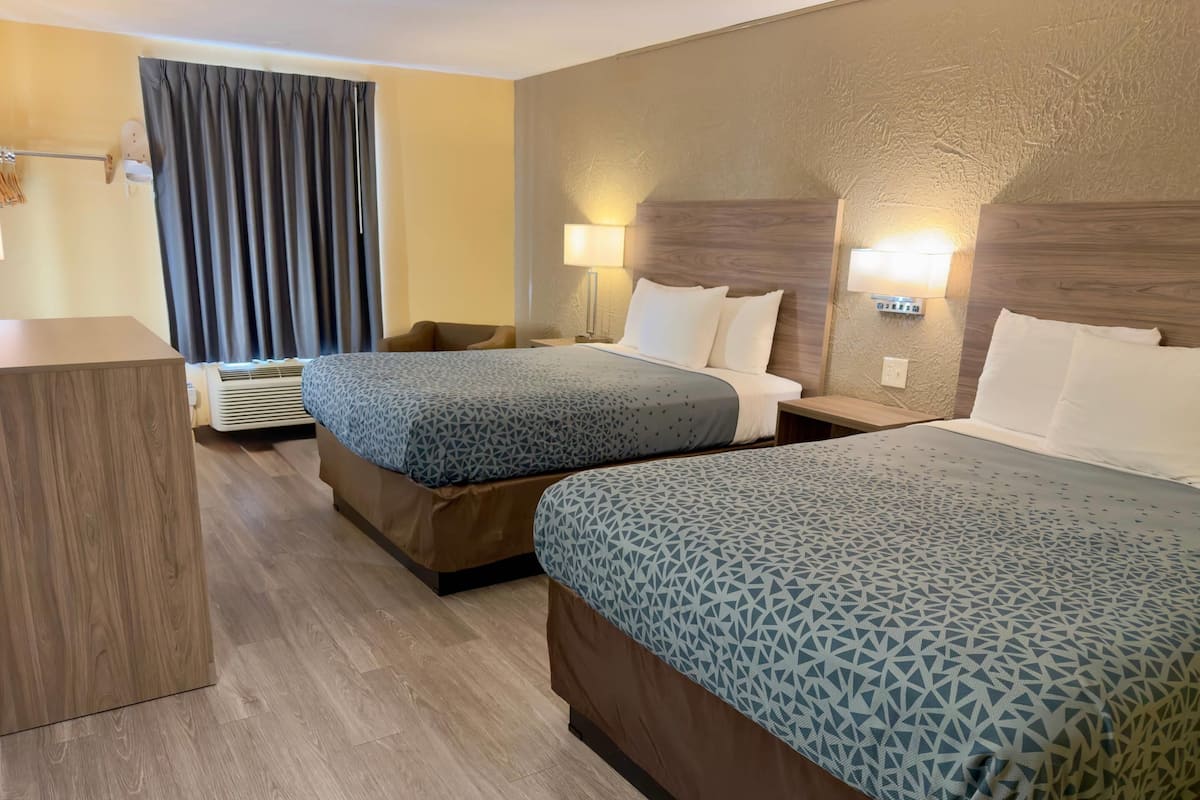 Une chambre d’hôtel avec deux lits, un bureau, une chaise, une lampe fixée au mur et un rideau.